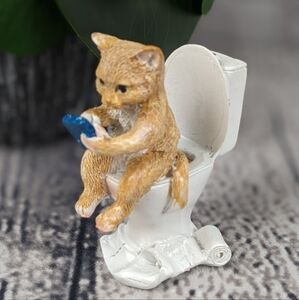 Orange ginger cat using phone while sitting on a toilet, feline statue figurine